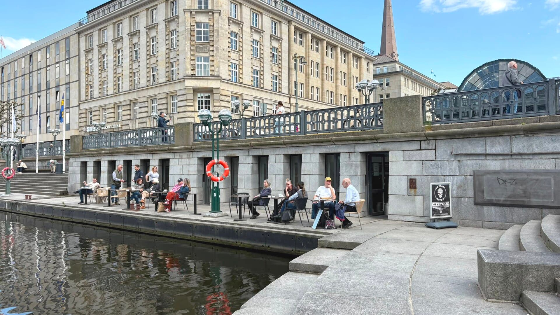 Die Terrasse am Wasser vor der Rathauspassage Hamburg an einem sonnigen Tag, Menschen sitzen an den Tischen